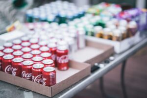 Latas de Coca-Cola y otras bebidas dispuestas en bandejas de cartón listas para distribución o venta.
