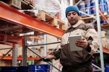 Trabajador en almacén utiliza tableta para registrar o verificar inventario en estanterías industriales.