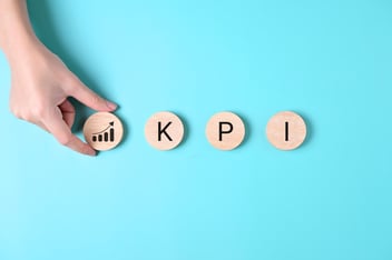 Mano colocando ficha de madera con gráfico de crecimiento junto a las letras KPI sobre fondo azul.