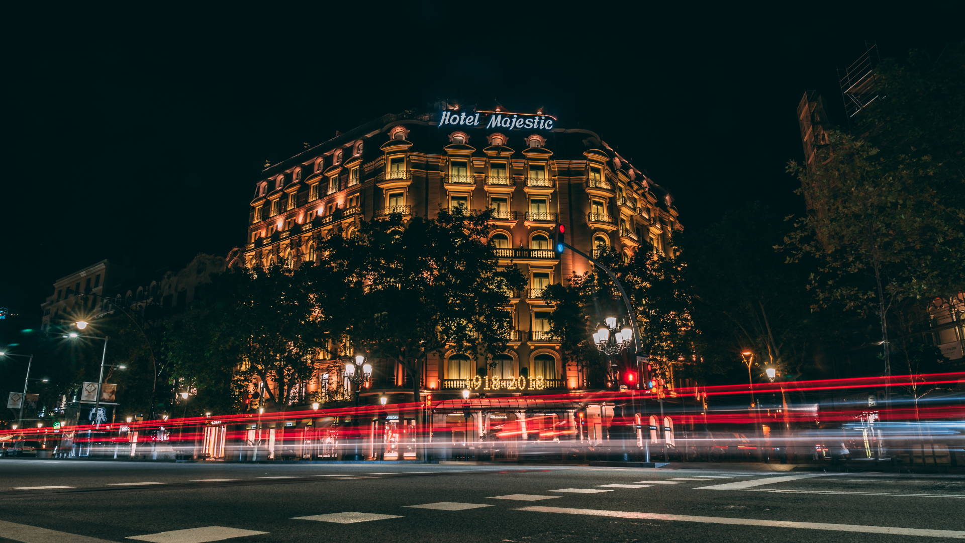 Vista nocturna del Hotel Majestic en el Passeig de Gràcia, España. La imagen muestra el movimiento acelerado de la ciudad con larga exposición de luces de vehículos, simbolizando el flujo de distribución y transporte en el sector de la hostelería.