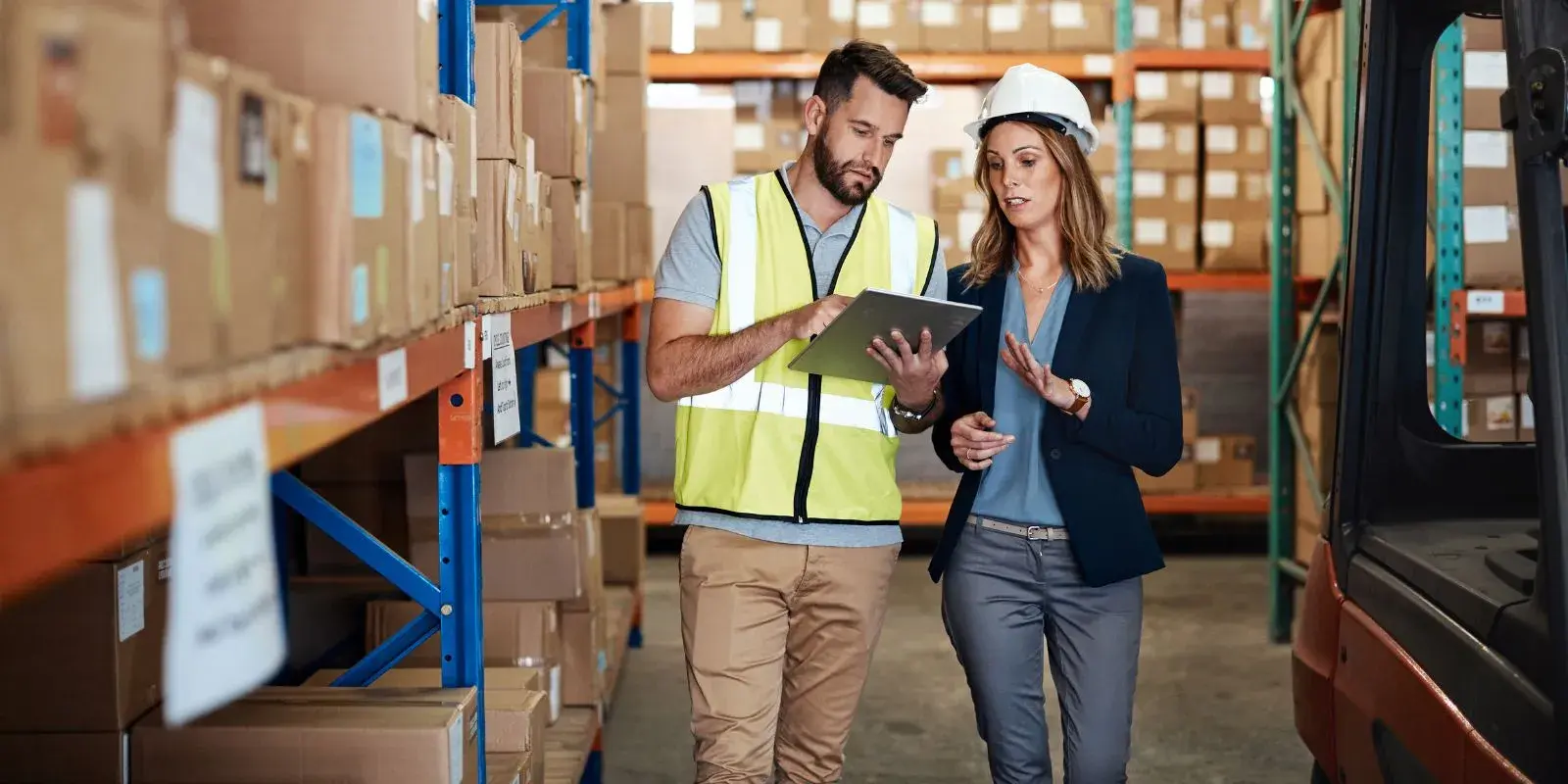 Dos personas revisan inventario en almacén, analizando datos logísticos en tableta para optimizar rutas y entregas.