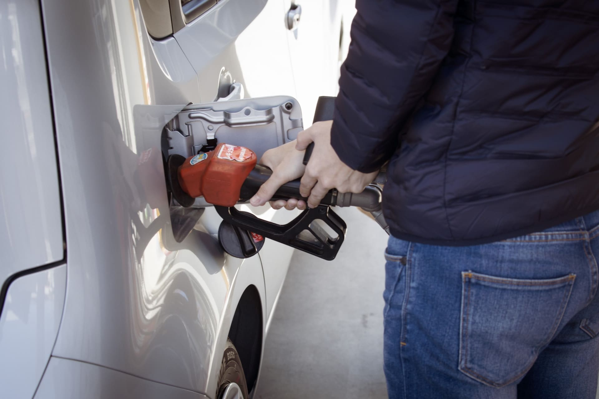 Persona cargando combustible en un automóvil en una estación de servicio, representando costos de transporte y consumo de combustible en logística.